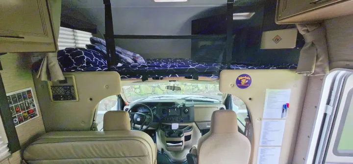 **RV rental** interior: Looking forward, showing the driver's cabin, cozy over-cab bunk bed with patterned bedding, and front seats.. Thor Four Winds 2022