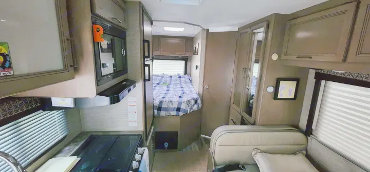 RV rental interior view: compact kitchen (microwave, stove), bed with blue plaid blanket, and a comfortable seating area.. Thor Four Winds 2022