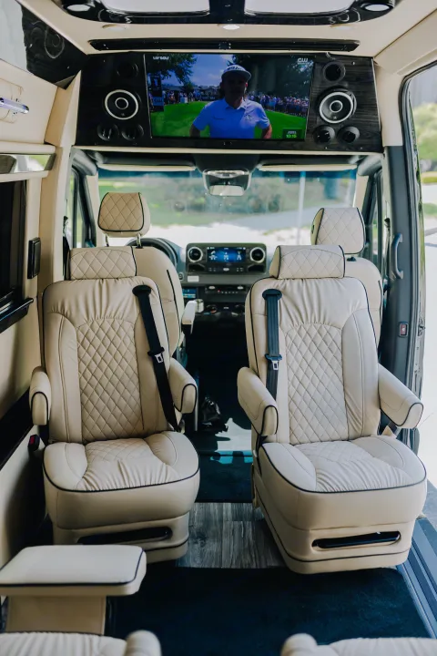 Inside a premium RV rental: two luxurious beige quilted captain's chairs face a TV showing golf. Enjoy top-tier comfort & entertainment.. Ultimate Toys Ultimate Coach 2023