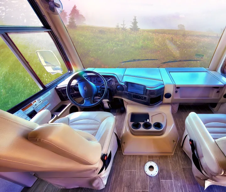 Spacious RV rental cockpit with cream driver's seat, steering wheel, and dashboard. Misty field view through windshield for road trips.. Thor Motor Coach Miramar 2020
