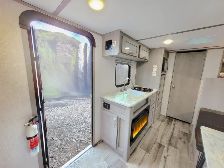 This RV rental features a compact interior with a full kitchen, electric fireplace, and a beautiful waterfall view from the open door.. Coleman Lantern 2023