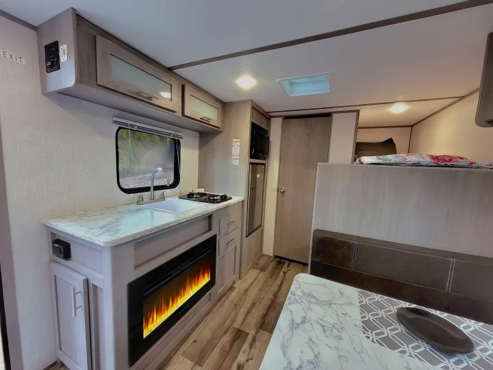 Modern RV rental interior featuring a kitchen with stove, sink, and electric fireplace, plus a cozy loft bed.. Coleman Lantern 2023