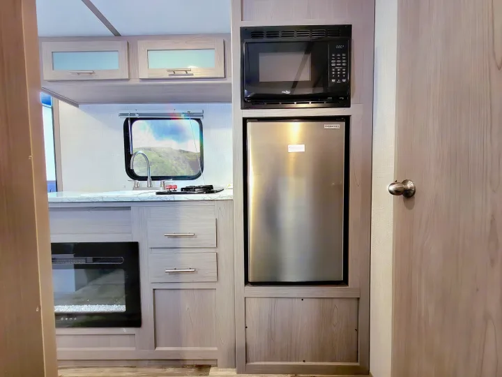 Modern RV rental kitchen with a microwave, refrigerator, two-burner stove, and an electric fireplace.. Coleman Lantern 2023
