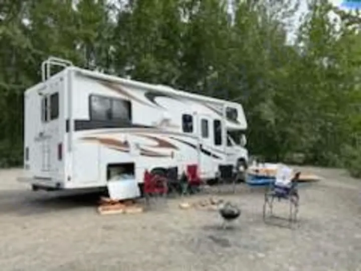 White motorhome RV rental parked for camping. Outdoor leisure setup with chairs & grill. Perfect for your next adventure.. Forest River Sunseeker 2012