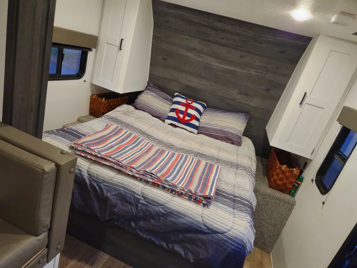 Cozy RV rental bedroom with striped bedding, anchor pillow, and cabinet storage. Perfect for travel!. Keystone RV Hideout 2021