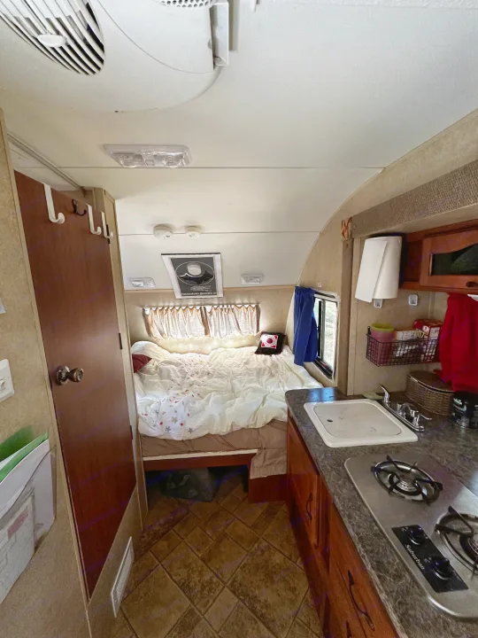 Interior of an RV rental: a compact living space featuring a bed with patterned sheets and a functional kitchen with a sink and stove.. R-Pod R-Pod Trailer 2011