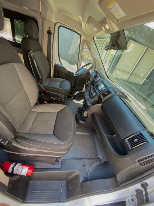 Front cabin of an RV rental, showing driver and passenger seats, dashboard, and a fire extinguisher for safety.. Winnebago Winnebago Solis P 2022