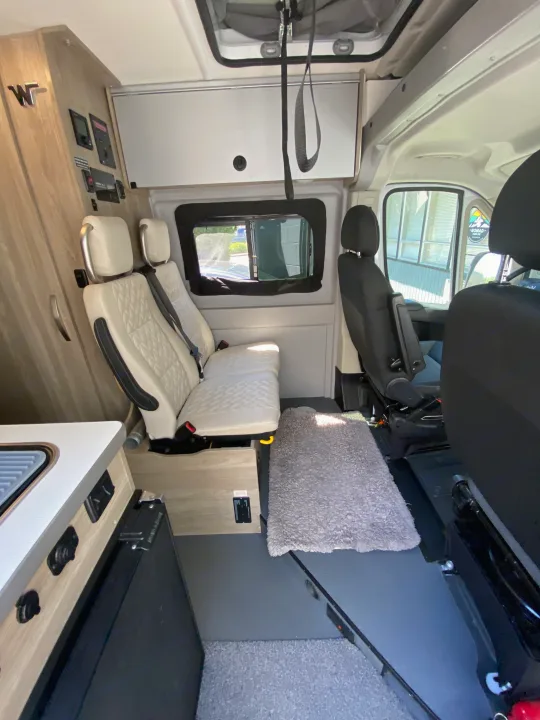 RV rental interior: cream quilted rear seats, black front seats, kitchenette, control panel, and overhead storage.. Winnebago Winnebago Solis P 2022