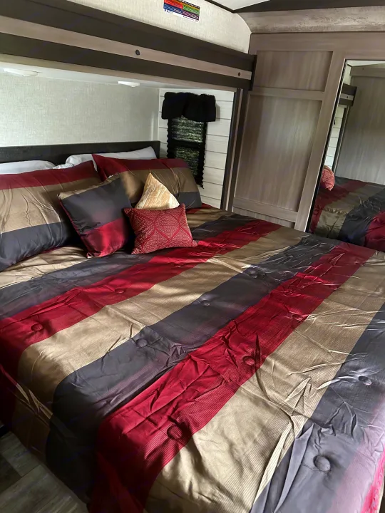 Comfortable RV rental bedroom featuring a striped bed in maroon, gray, and tan. Perfect for your travels!. Crossroads RV Sunset Trail Super Lite 2023