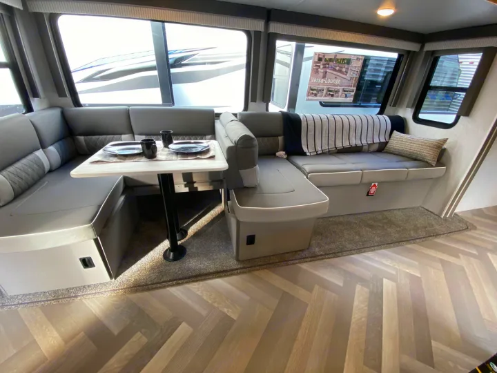 Modern gray L-shaped lounge/dinette area in an RV rental, featuring a table, large windows, and sleek flooring for comfortable travel.. Forest River Salem 2022