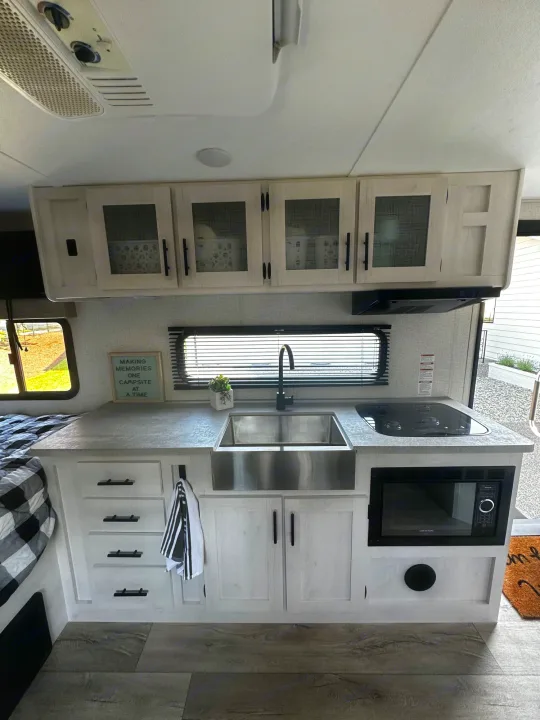 Modern RV rental kitchen with light wood cabinets, a sink, built-in stovetop, and microwave.. Dutchmen Coleman Rubicon 2021