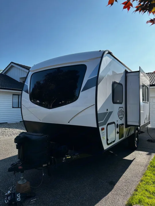 A white travel trailer, a potential RV rental, parked on a driveway with an extended slide-out. Ready for adventures!. Dutchmen Coleman Rubicon 2021