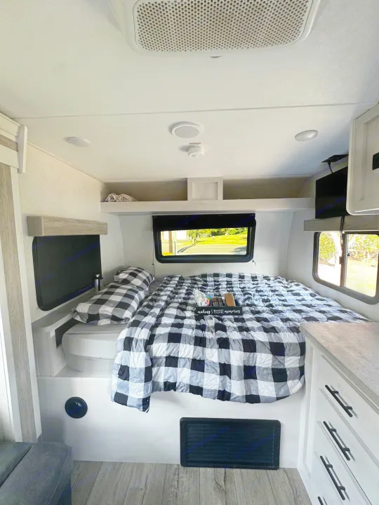 Cozy RV rental bedroom with black and white buffalo check bedding. The modern space features windows showing outdoor scenery, perfect for making memories.. Dutchmen Coleman Rubicon 2021