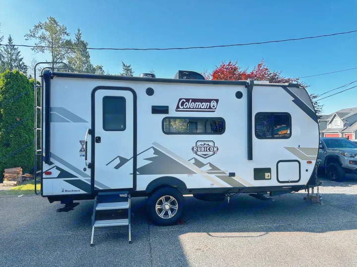 A white Coleman Rubicon travel trailer is parked on asphalt with steps down, ideal for your next RV rental adventure.. Dutchmen Coleman Rubicon 2021