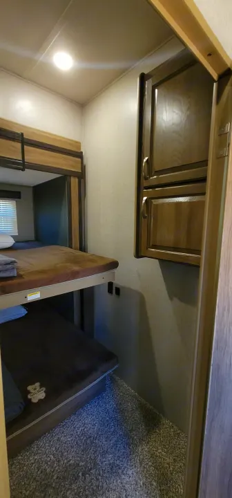 RV rental interior: Overhead wooden cabinets, a bunk bed area with stacked mattresses, and a carpeted floor with a pet bed are visible.. Atlas Atlas Fifth Wheel 2019