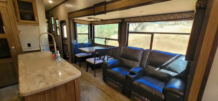 Inside an rv rental: a cozy living space featuring a kitchen island, dining area, and plush recliners by large windows.. Atlas Atlas Fifth Wheel 2019