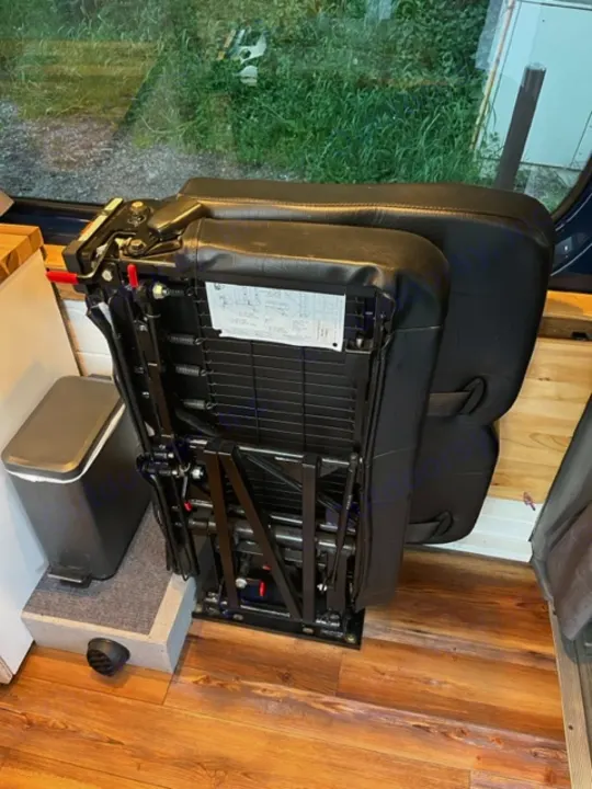 RV rental interior: A black rear seat showing its metal base and recline mechanism. A small heater sits nearby on the wood floor.. Mercedes Sprinter 2016