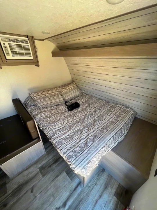 Cozy RV rental bedroom featuring a patterned bed, mounted AC unit, and built-in storage, ideal for travel and camping.. Dutchmen Coleman Lantern LT 2023