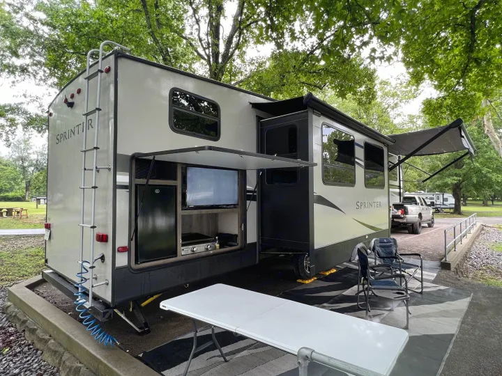 This spacious rv rental, with its outdoor kitchen and extended awnings, is comfortably set up at a shady campsite.. Keystone RV Sprinter Campfire Edition 2020