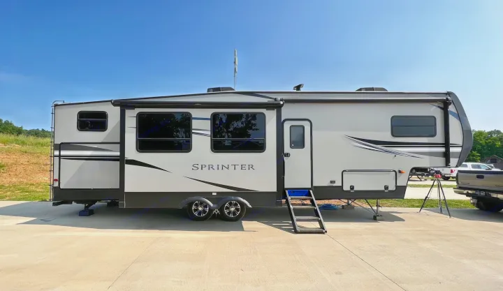 Modern light gray Sprinter travel trailer, an ideal RV rental, parked on concrete under a clear sky. Steps are down, antenna up.. Keystone RV Sprinter Campfire Edition 2020