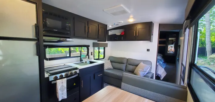 Stylish RV rental interior: Full kitchen with dark cabinets, microwave, stove, and sink. Cozy living area with sofa and dining space.. Keystone RV Springdale 2022