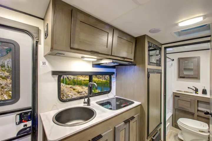 Modern RV rental interior, showcasing a compact kitchen with sink, cooktop, microwave, and a functional bathroom area.. Heartland RVs Mallard Pathfinder 2021