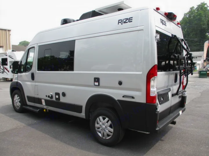Side view of a silver RIZE camper van, featuring a bike rack, solar panels, and utility hookups, ideal for rv rental.. Thor Motor Coach Rize 2023