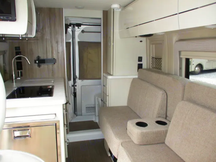 Modern RV rental interior showing a kitchen (sink, cooktop, fridge), comfy sofa with cupholders, and overhead cabinets.. Thor Motor Coach Rize 2023