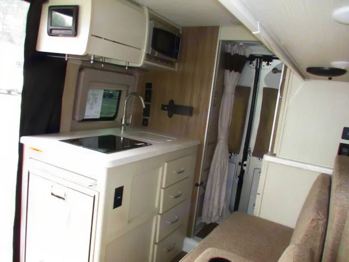 Compact rv rental interior with a modern kitchen (sink, cooktop, fridge), microwave, bathroom, and seating area.. Thor Motor Coach Rize 2023