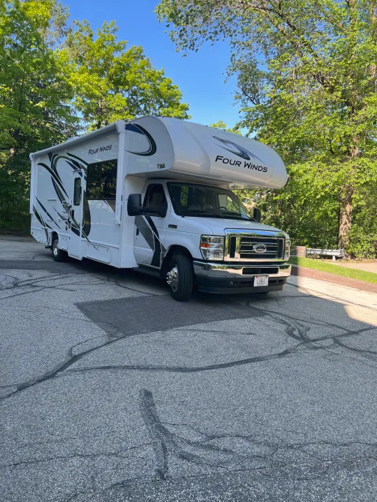 White Thor Motor Coach Four Winds Class C rv rental, parked on asphalt with trees & blue sky.. Thor Four Winds 2021