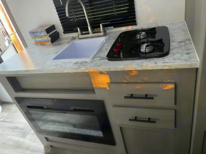 This RV rental's kitchen features a sink, dual cooktop, electric fireplace, and storage drawers.. Dutchmen Coleman Lantern LT 2023