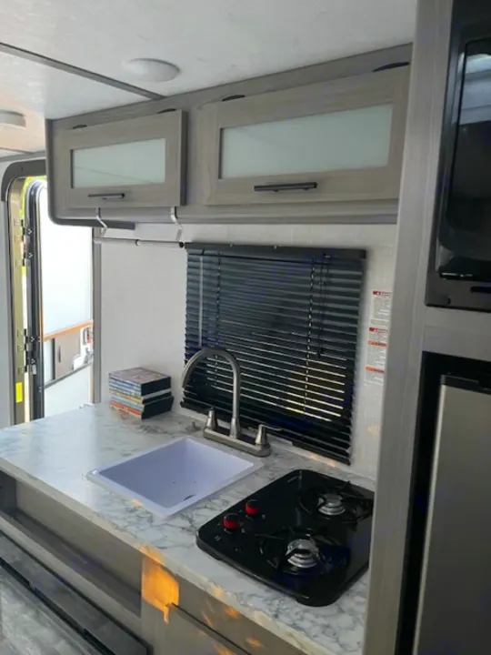 Compact rv rental kitchen: sink, two-burner stove, and overhead cabinets for cozy travel meals.. Dutchmen Coleman Lantern LT 2023