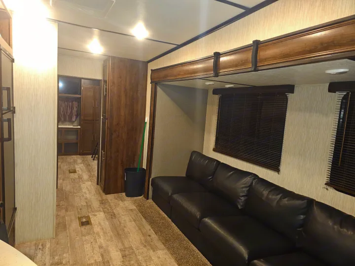 Spacious RV rental interior: a comfy black leather sofa, light wood-look floors, and modern cabinetry define this living space.. Crossroads RV Volante 2019