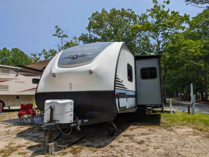 An RV rental travel trailer is parked at a sunny campsite with utility hookups and trees, ready for outdoor adventure.. Forest River Surveyor 2017