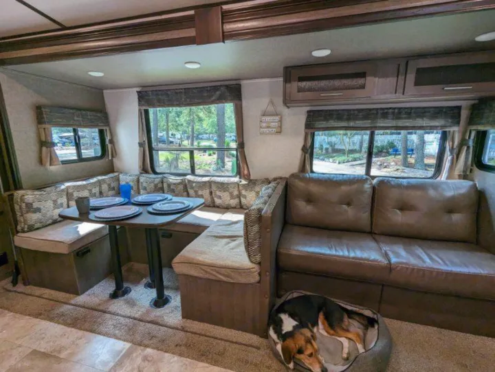 Inside an RV rental: a warm living space with a U-shaped dinette, comfy sofa, and a dog resting in its bed.. Forest River Surveyor 2017