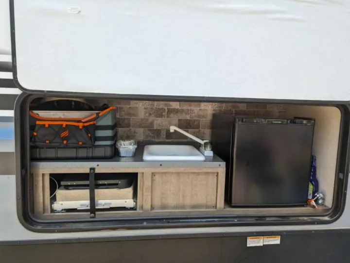 Explore this RV rental's outdoor kitchen! Features a sink, mini-fridge, and pull-out grill for convenient camping.. Forest River Surveyor 2017