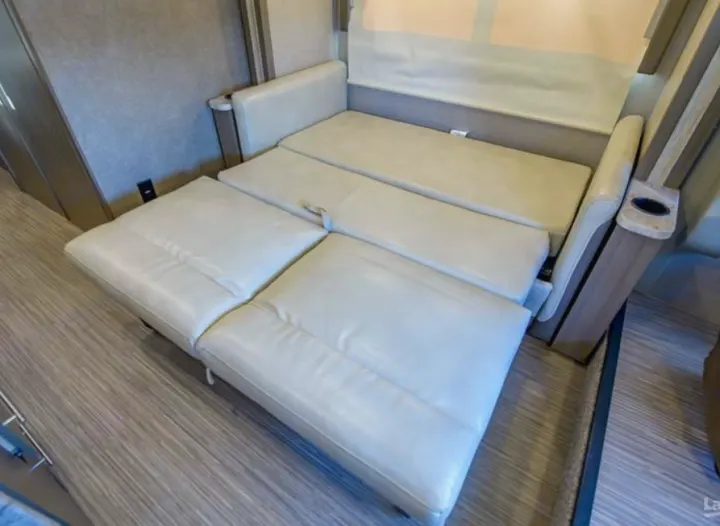An RV rental's cream sofa sleeper extends, demonstrating versatile seating and sleeping in a compact space.. Thor Vegas 2018