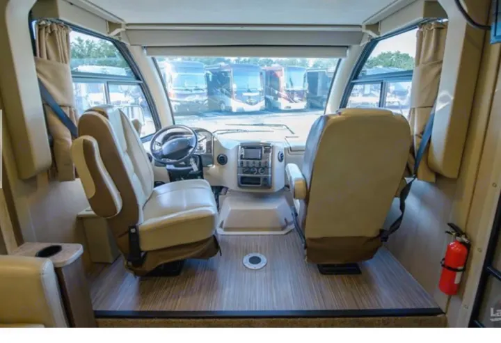 View of an RV rental's front interior, showcasing comfortable captain's chairs, a steering wheel, dashboard, and spacious cabin.. Thor Vegas 2018