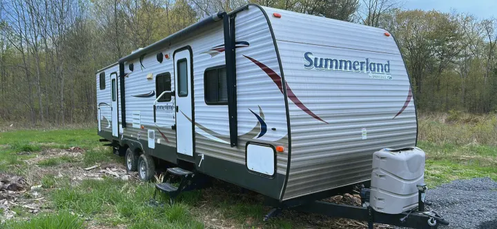 Summerland travel trailer RV, light grey with red/blue graphics, parked outdoors. Great for your next rv rental adventure.. Keystone RV Summerland 2015