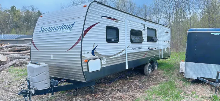 Summerland travel trailer for RV rental, parked outdoors among trees and logs. A great recreational vehicle for your next adventure.. Keystone RV Summerland 2015