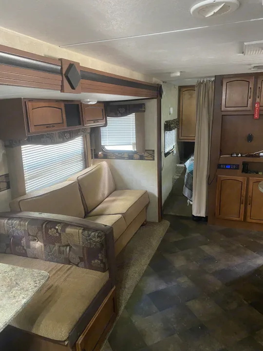 RV rental's inviting living space with sofa, dinette, overhead cabinets, and dark vinyl flooring. Leads to a private bedroom.. Keystone RV Summerland 2015