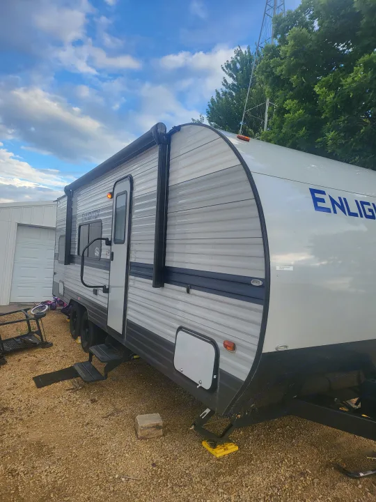 White and grey travel trailer RV rental, parked on gravel with an extended awning and visible steps.. Gulf Stream Enlighten 2021