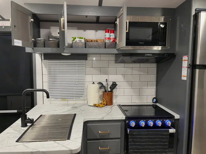 This RV rental features a modern, compact kitchen with a sleek sink, stove, microwave, and well-organized gray cabinets for travel.. Keystone RV Bullet Ultra Lite 2022