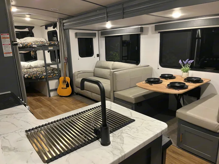 Modern RV rental interior with bunk beds, sofa, kitchen counter, and dining table set for four. Ready for travel comfort.. Keystone RV Bullet Ultra Lite 2022