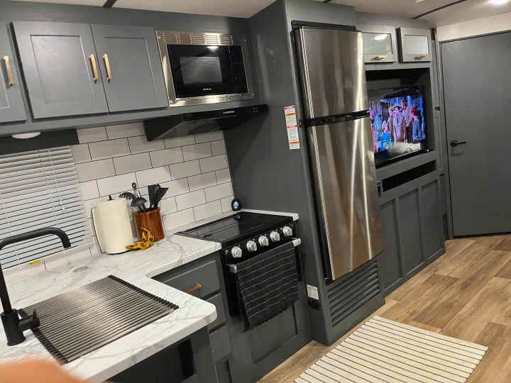 RV rental: Modern camper kitchen with grey cabinets, stainless steel fridge/microwave, sink, and a TV.. Keystone RV Bullet Ultra Lite 2022
