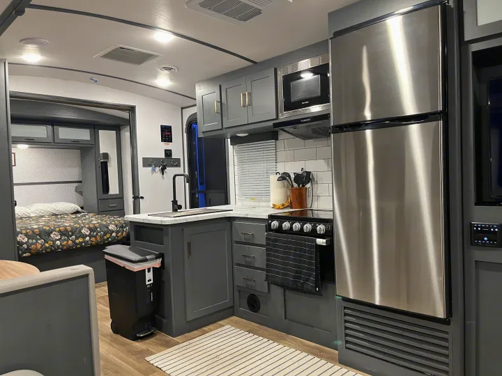 This modern RV rental interior features a compact kitchen with stainless steel appliances, a sink, and a view into the cozy bedroom.. Keystone RV Bullet Ultra Lite 2022