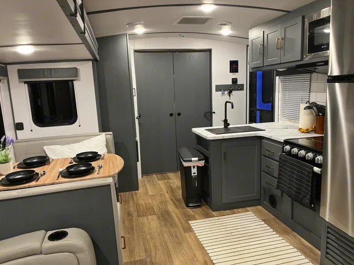 Modern RV rental interior with a fully equipped kitchen, dining area, and ample storage. Sleek grey cabinets and wood-look flooring enhance comfort.. Keystone RV Bullet Ultra Lite 2022