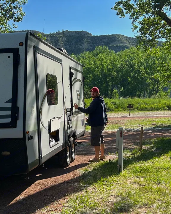 Man with red cap prepares his RV rental at a scenic mountain campsite (site 315).. Forest River Rockwood Roo 2019