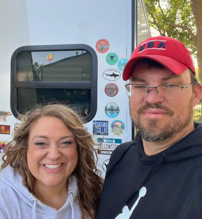 Happy couple by their RV rental, featuring stickers from national parks like Yellowstone & Glacier. Mountains are calling!. Forest River Rockwood Roo 2019