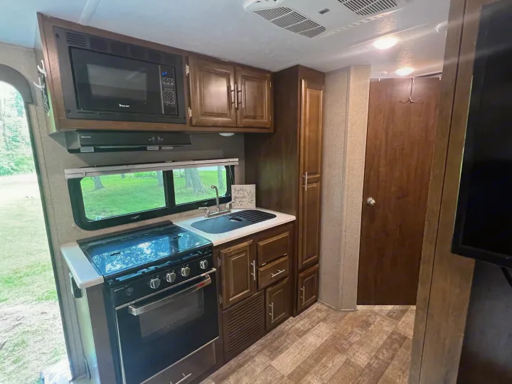 Modern RV rental kitchen showcasing a microwave, gas stove with oven, sink, and ample dark wood cabinetry. Ideal for travel.. Forest River Rockwood Roo 2019